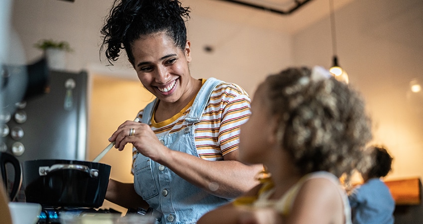 Vrouw in denim schort serveert eten aan kinderen in moderne keuken