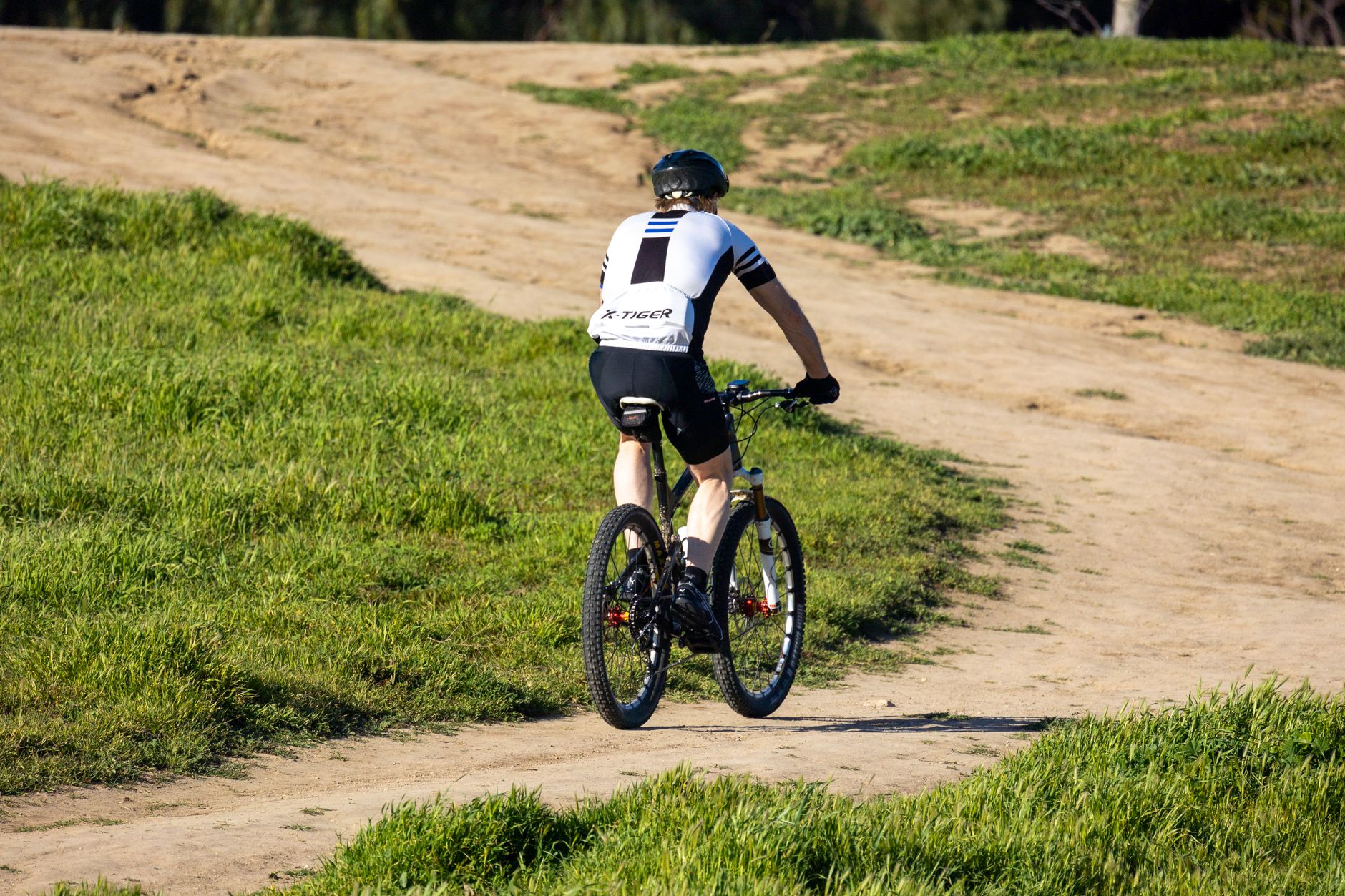 Single cyclist riding on a dirt path through green vegetation wearing white and black cycling gear