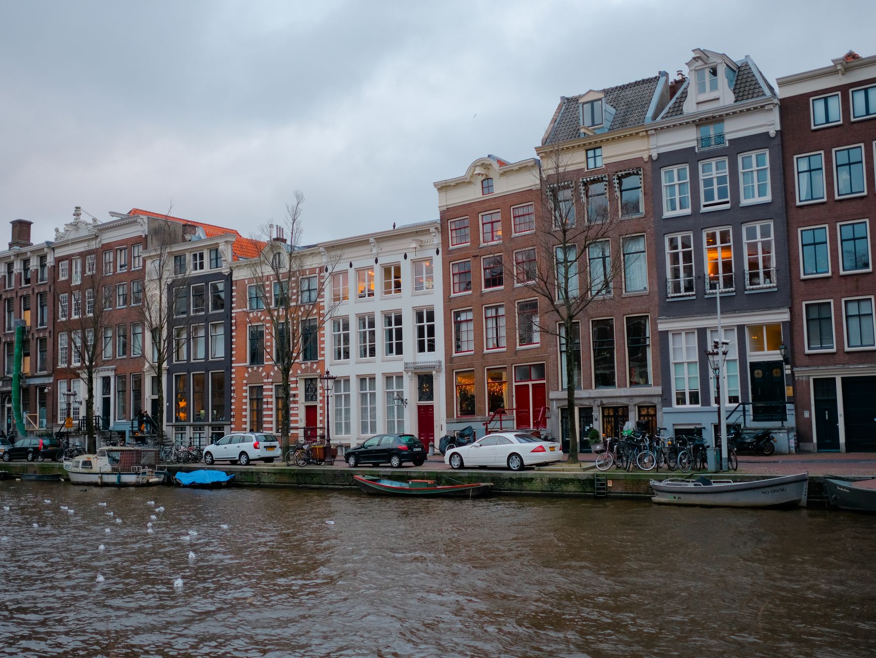 Contemporary color photograph of colorful historic buildings reflected in an Amsterdam canal with bicycles and parked cars along the waterfront