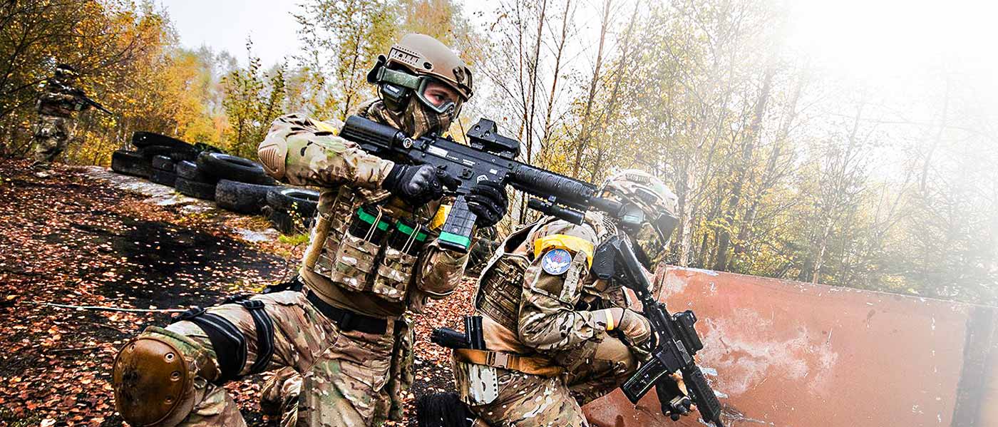 Zwei bewaffnete Spieler in Tarnanzügen und Schutzausrüstung in herbstlichem Waldgelände beim Paintball.