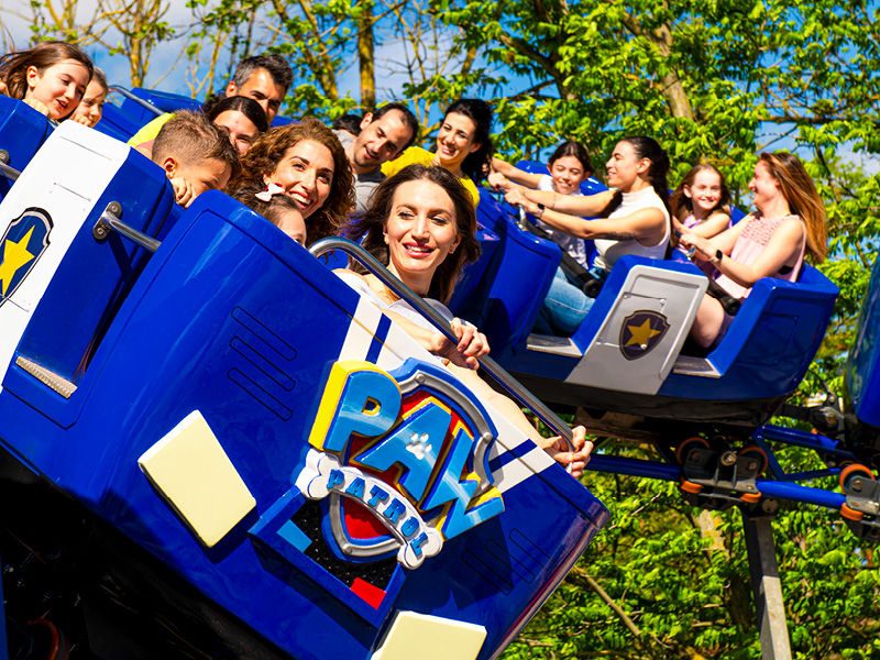 Gruppo di visitatori felici seduti su un'attrazione blu e gialla in un parco