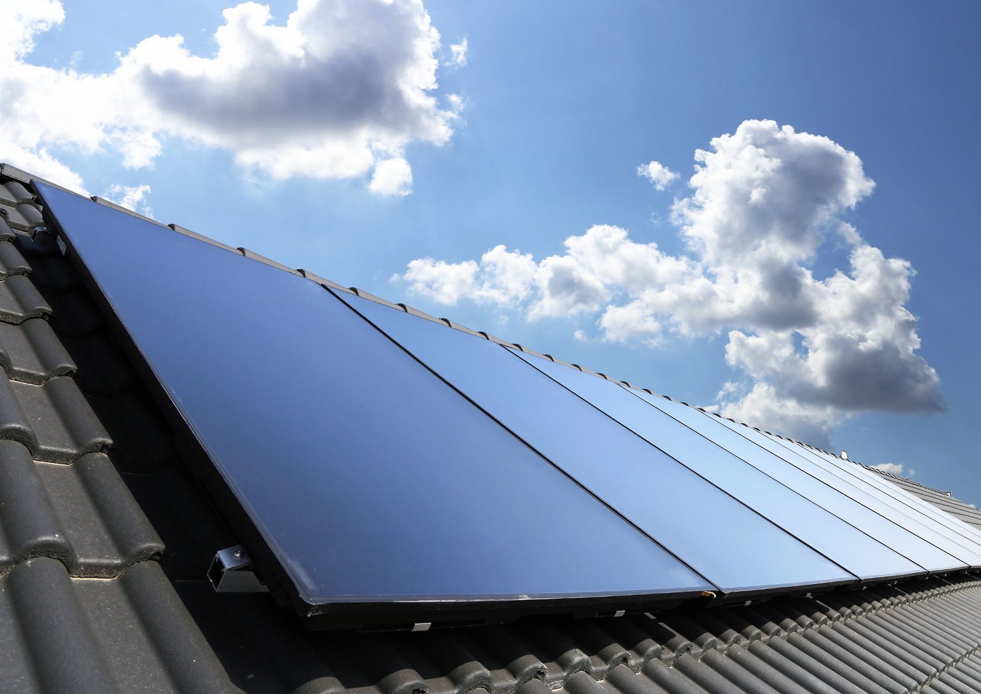 Zonnepanelen op dak tegen blauwe lucht met witte wolken