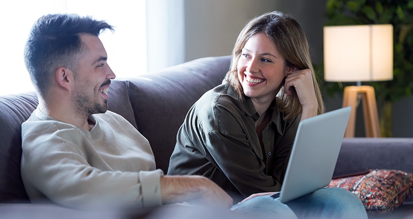 Man en vrouw zitten op grijze bank en kijken naar laptop scherm