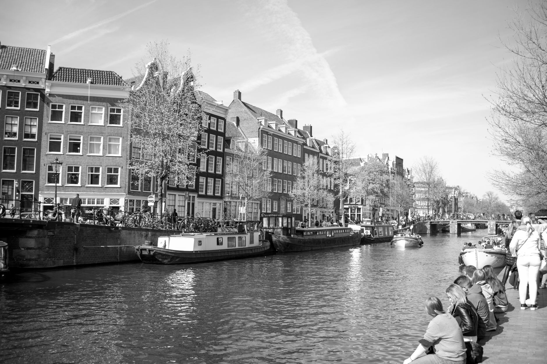 Black and white photograph of a canal in Amsterdam with historic buildings lining the waterfront and boats docked along the water
